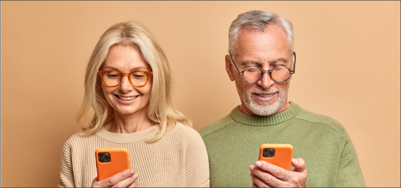 Casal maduro sorrindo usando celulares conectados aos aparelhos auditivos